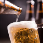Glass bottles of beer with glass and ice on dark background