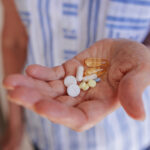 In the hands of an elderly woman, a handful of various pills and vitamins.
